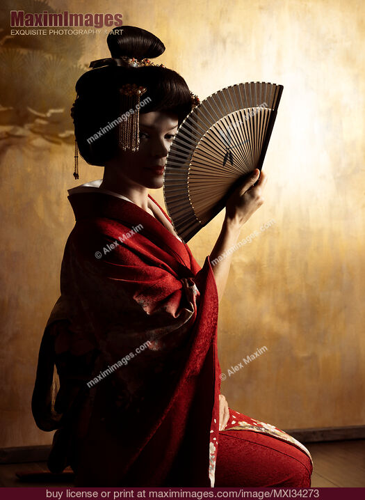 Stock photo of Mesmerizing portrait of beautiful caucasian lady, Japanese geisha with hand fan casting shadows on her face against golden wall Buy commercial use license at MaximImages