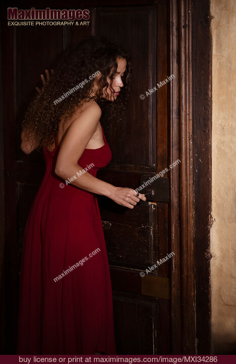 Stock photo of Woman in red dress cautiously listening to the door while opening the lock Buy commercial use license at MaximImages