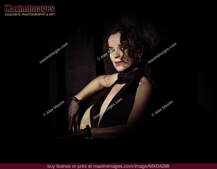 Stock photo of Dramatic portrait of beautiful mysterious femme fatale lady dressed in black wearing veiled hat covering her face Buy commercial use license at MaximImages