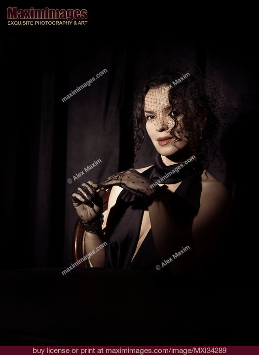 Stock photo of Portrait of beautiful mysterious femme fatale lady dressed in black wearing veiled hat taking off her gloves Buy commercial use license at MaximImages