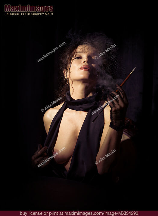 Stock photo of Beautiful seductive femme fatale lady in black dress and veil exposing her breast and exhaling cigarette smoke Buy commercial use license at MaximImages