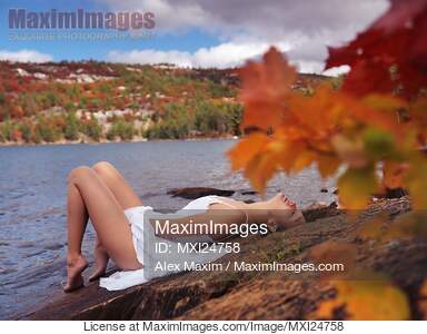 Young woman in white dress lying on shore of lake in fall... preview image