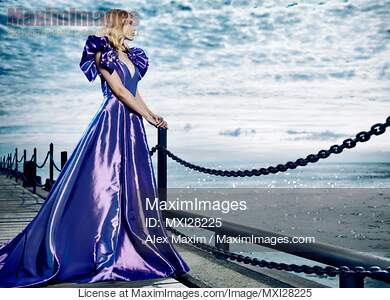 Woman wearing beautiful long blue dress standing at waterfront... preview image