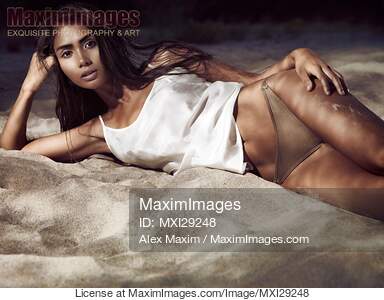 Sexy beautiful exotic woman lying on beach sand in dramatic light... preview image