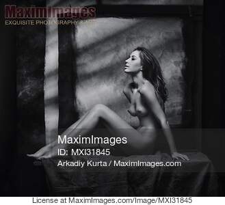 Fine art nude woman sitting naked on a posing table in artist studio... preview image