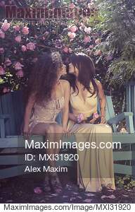 Cute lesbian couple kissing on a bench in a garden... preview image