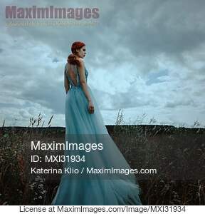 Young red haired woman in a long blue dress standing...... preview image