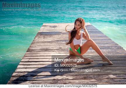 Sexy woman sitting on a pier in a one-piece swimsuit with...... preview image