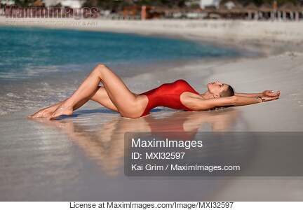 Woman in sexy red swimsuit lying on a sandy shore of...... preview image
