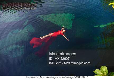 Woman in beautiful red dress lying on clear blue water...... preview image