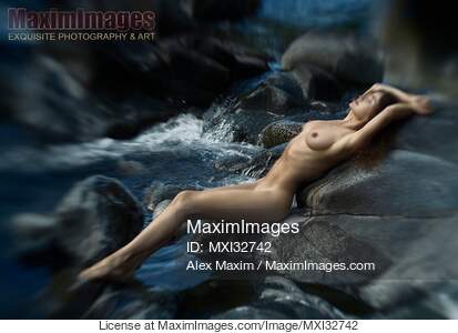 Woman lying naked on dark river rocks in rushing water...... preview image
