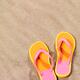 Pair of bright orange flip flops on beach sand... (thumbnail)