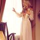 Beautiful blond woman in night gown looking out of the window... (thumbnail)