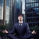 Businessman meditating with office buildings behind him... (thumbnail)