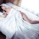 Beautiful woman sleeping naked in bed covered with white sheets lit by... (thumbnail)