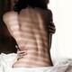 Naked back of a woman sitting on a bed in dramatic light... (thumbnail)