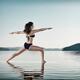 Woman practicing yoga on the water doing Warrior pose over blue sky... (thumbnail)