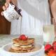 Woman pouring maple syrup on pancakes... (thumbnail)