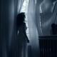 Woman standing at window in dark room in dim sunlight... (thumbnail)