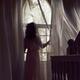 Woman in dress standing by the window in dark house... (thumbnail)