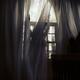 Woman standing behind the curtains at window in dark room... (thumbnail)