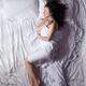 Young woman sleeping in bed covered with a sheet in morning light... (thumbnail)