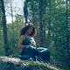 Woman in green dress sitting on rocks in the nature with a flower in h... (thumbnail)