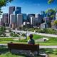 Woman sitting on a bench in Sunnyside Bank Park with Calgary downtown... (thumbnail)