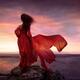 Woman in red dress flying in the wind looking at the ocean in sunset... (thumbnail)