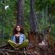 Young woman resting meditating in forest sitting against tree trunk in... (thumbnail)