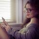 Woman with an iPhone in her hands sitting by the window texting... (thumbnail)