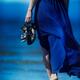 Woman in blue dress walking barefoot on ocean beach sand... (thumbnail)