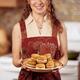 Smiling young woman in an apron holding a plate of freshly baked home-... (thumbnail)