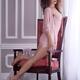 Girl in sheer pink lingerie nightwear leaning against a chair by the w... (thumbnail)