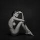 Art nude side view of a woman sitting naked in studio with black backg... (thumbnail)