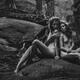 Two beautiful nude young women sitting in a forest among trees leaning... (thumbnail)