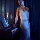 Woman in a long night gown standing thoughtfully by the piano in a dar... (thumbnail)