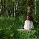 Woman practicing sitting meditation leaning against a tree trunk in a... (thumbnail)