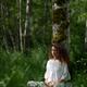 Woman practicing sitting meditation leaning against a birch tree in gr... (thumbnail)