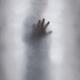 Ghostly mysterious man touching glass barrier with his hand dream-like... (thumbnail)