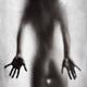 Rear view of nude sexy woman in a provocative pose standing behind wet... (thumbnail)