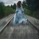 Woman in a long dress walking along railroad tracks in the wind... (thumbnail)