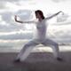 Woman in sheer white clothes practicing Tai Chi on the ocean shore in... (thumbnail)