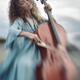 Beautiful young woman in a blue vintage dress passionately playing cel... (thumbnail)