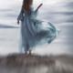 Woman in a long elegant dress flying in the wind standing on ocean sho... (thumbnail)