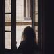 Back of a woman looking out of an open window standing inside a dark h... (thumbnail)