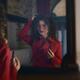 Woman in a red coat and glasses standing in front of a mirror holding... (thumbnail)