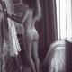Black and white boudoir portrait of a nude young woman dressing up in... (thumbnail)