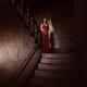 Woman in red dress standing like a ghost on dark house staircase looki... (thumbnail)