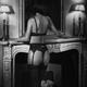 Sexy woman back in lingerie and stockings by mantelpiece with a man si... (thumbnail)